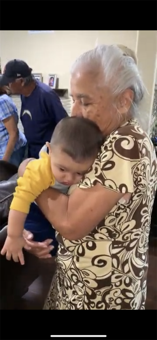 A grandmother hugs her grandchild warmly amid family at a busy market.
