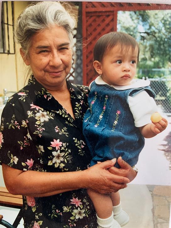 Elderly woman happily cradles a curious toddler in a vibrant neighborhood.