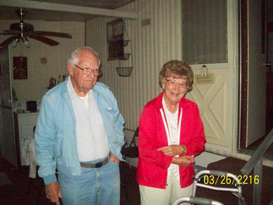 Two elderly individuals smile and interact inside a cozy setting during a social gathering.