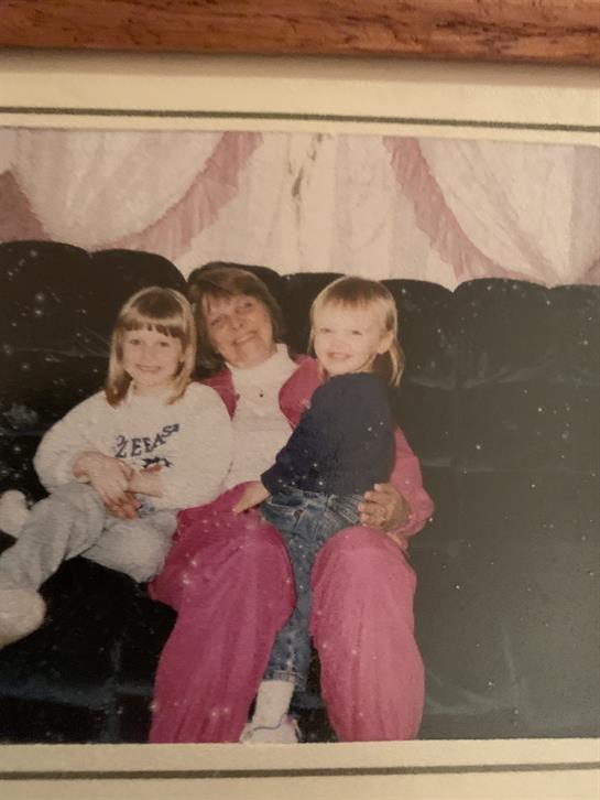 Two young girls are happily seated with a woman on a couch, creating a warm family moment.