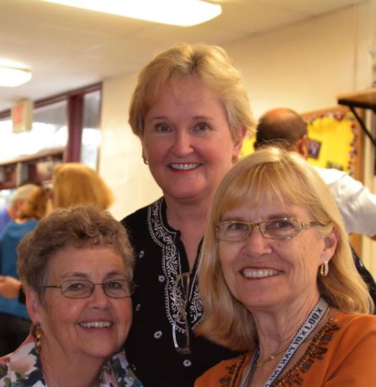 Three women happily pose together amid lively conversation at a social gathering.