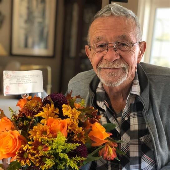Senior man with glasses enjoys a colorful bouquet of autumn flowers in a warm home environment.