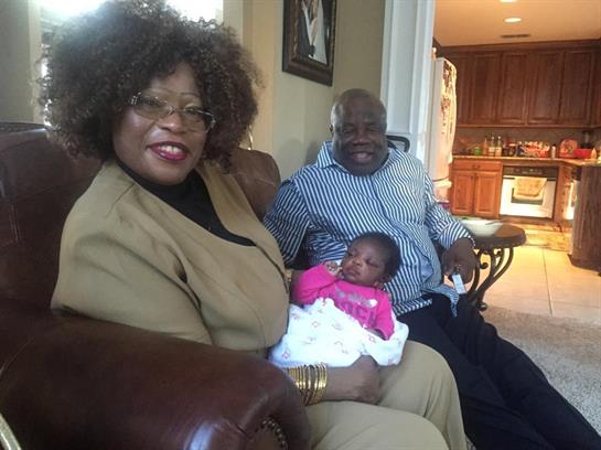 Two adults sit comfortably with a baby in a cozy living room filled with warmth and affection.