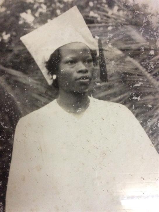 A woman in a graduation cap and gown stands proudly among greenery, embodying hope.