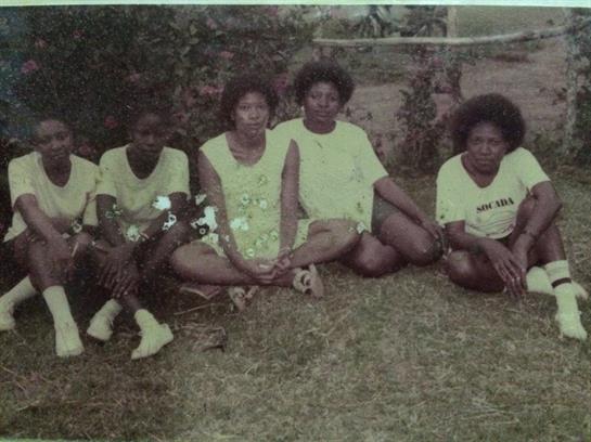 Five women relax on the grass, enjoying each other's company in a casual outdoor setting.