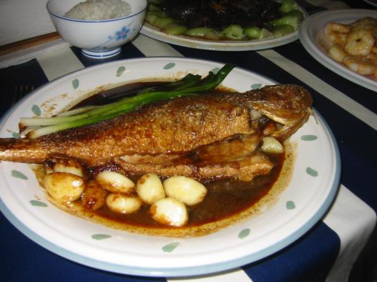Crispy fish garnished with green onions rests on a plate, accompanied by small eggs in rich sauce.