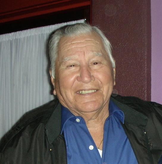A man with white hair enjoys a cheerful moment at a lively gathering, surrounded by warm colors.