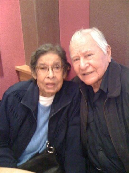Elderly couple sits closely together in a comfortable setting, sharing a joyful moment.