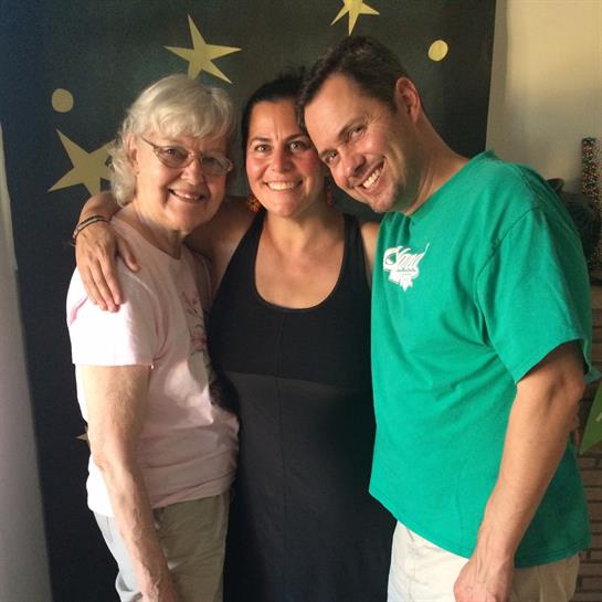 Three people smile and embrace, celebrating joy in a warm, inviting home.