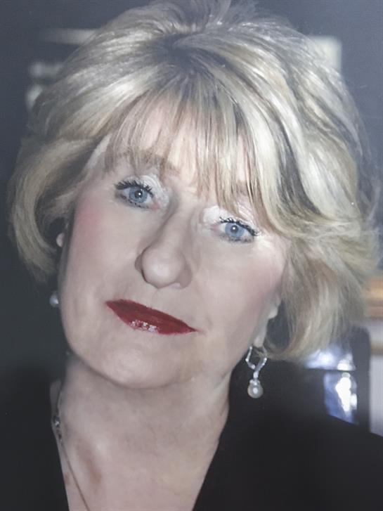 A woman with blonde hair styled elegantly poses with red lipstick in a softly lit room.
