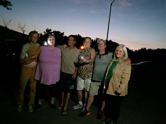 Group of friends enjoying an evening gathering with candles as the sun sets behind trees.