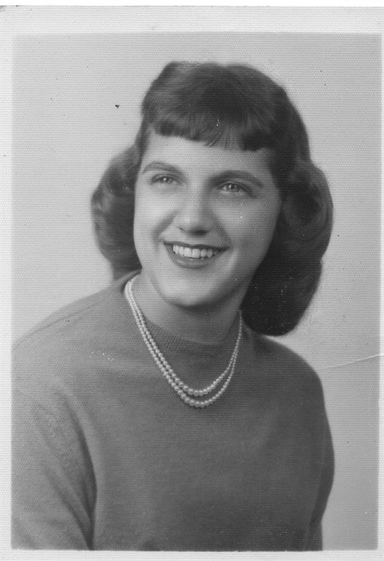 A joyful young woman poses for a studio portrait, wearing a sweater and pearls, with soft curls.