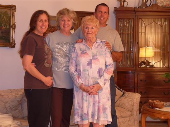 Four family members stand together in a warm living room, smiling and enjoying each other's company.