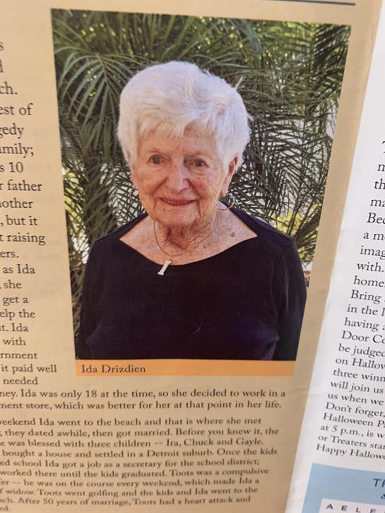 An elderly woman smiles warmly while standing in a lush garden, showcasing her rich history.