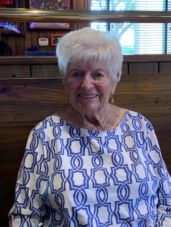 A happy elderly woman wearing a patterned shirt enjoys her time at a cozy indoor location.