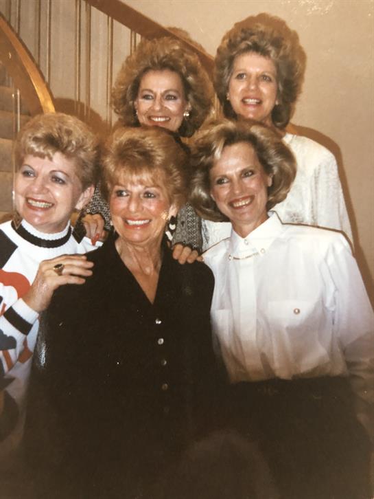 Six women sharing smiles and laughter while gathered together during a joyful event.