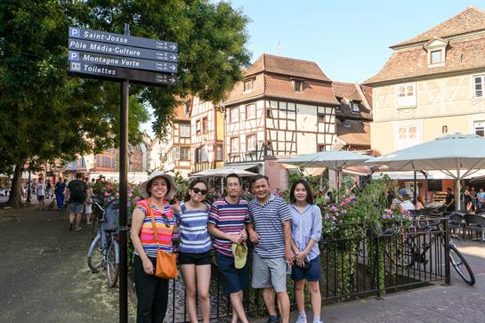Friends pose together in a picturesque town square with historic buildings and greenery.