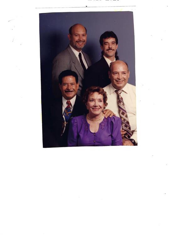 Five adults in formal attire smile together in a studio, showcasing their family ties.