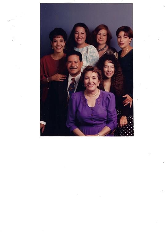 A group of eight individuals gathers in a studio, smiling and posing for a joyful family portrait.
