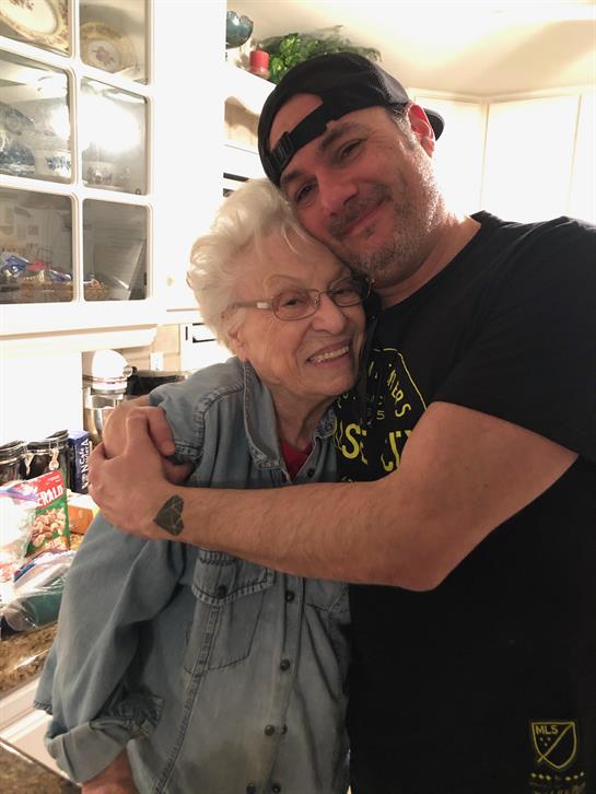 A man and an elderly woman are sharing a warm embrace in a cozy kitchen filled with food.