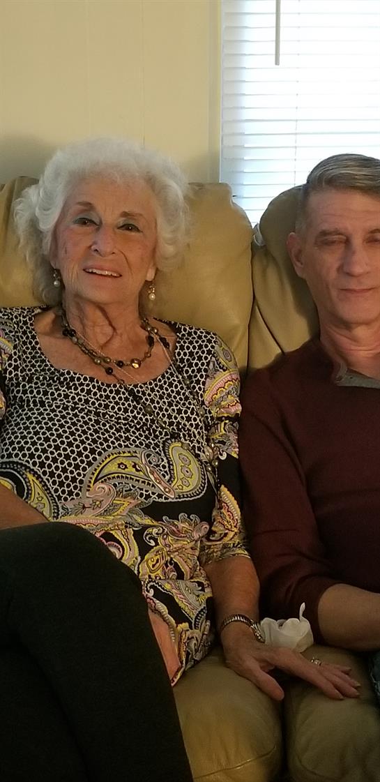 An elderly couple is sitting together on a comfortable couch in a warm living room.