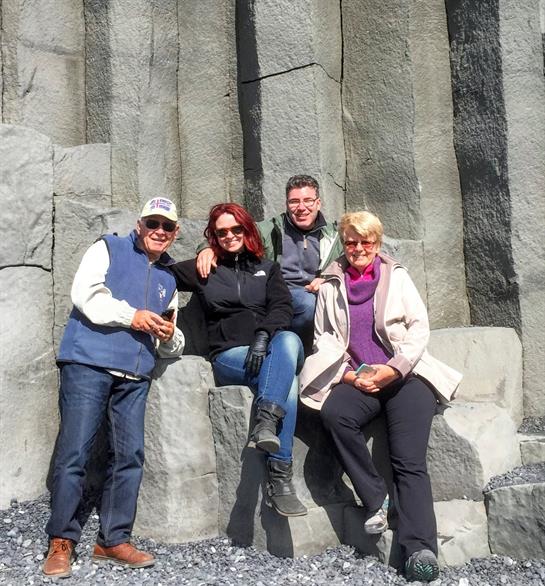 Four friends gather by natural basalt columns, engaging in friendly conversation and laughter.