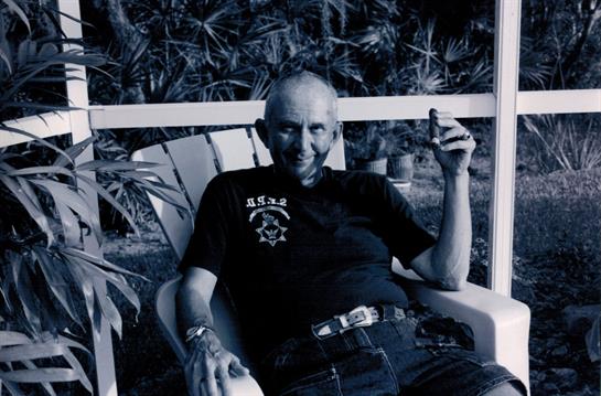 Man sits comfortably in a chair, enjoying a drink while surrounded by greenery.