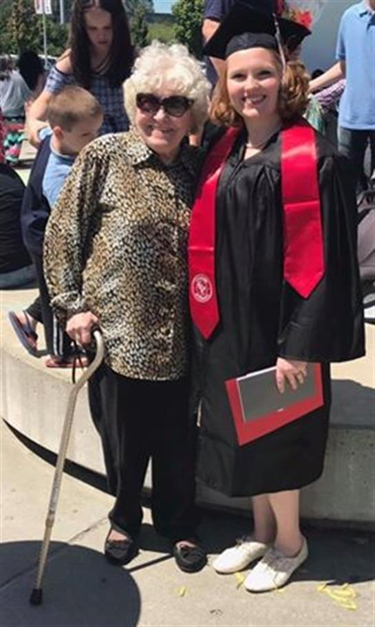 Graduate in cap and gown poses joyfully with grandmother during outdoor ceremony.