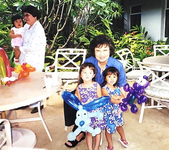 Children are joyfully holding balloon animals while adults interact in a vibrant garden.