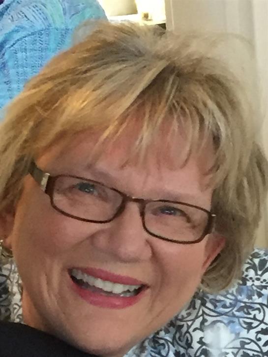 A joyful woman with glasses shares laughter and warmth with friends in a delightful setting.