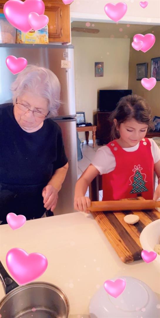 Grandmother and granddaughter work together to roll dough in a cozy kitchen while baking.