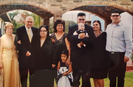 A group of eight people dressed in formal black attire stands together, smiling happily.