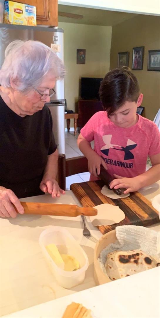 An elderly woman and a young boy are making dough for cooking in the kitchen.