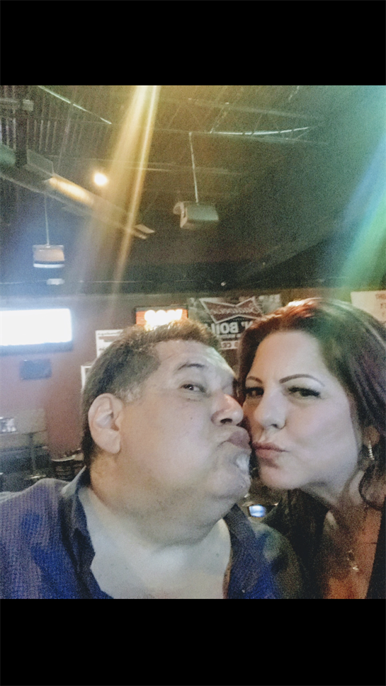 Couple shares a fun and affectionate moment while posing for a selfie in a bar.