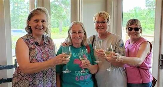 Four women joyfully toast with glasses of sparkling drink, enjoying a lively moment indoors.