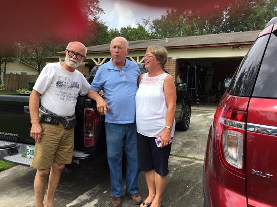 Three friends share a cheerful moment in a driveway, enjoying their time together outdoors.