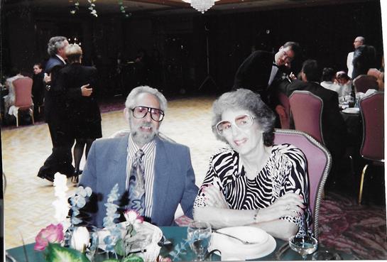 Older couple seated at a table, smiling and dressed for a special celebration in a banquet hall.
