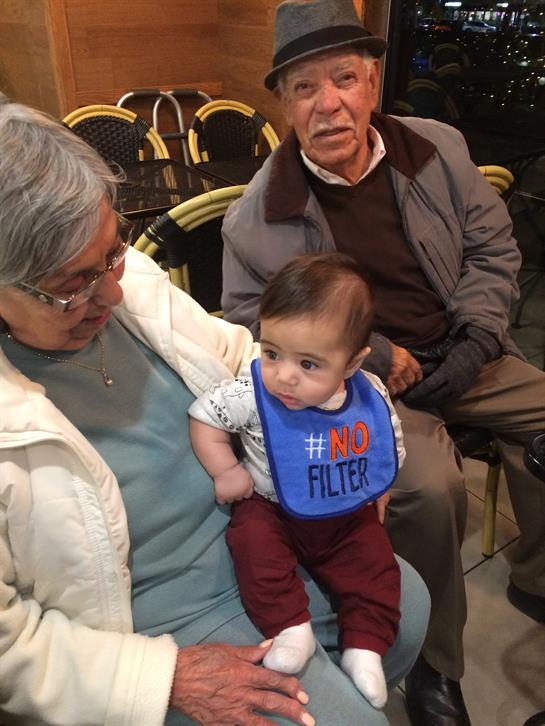 An elderly couple admires their baby, seated together in a warm gathering during the evening.