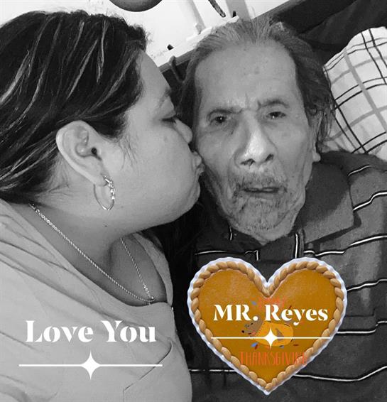 A woman affectionately kisses an elderly man while sharing a warm moment together indoors.