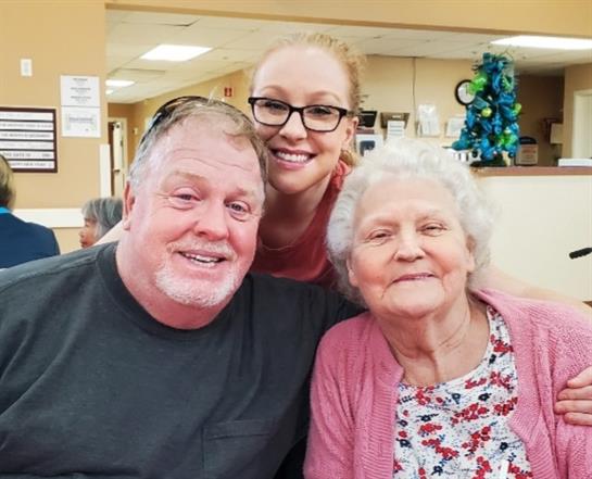 Three family members smile together happily in a welcoming indoor environment.