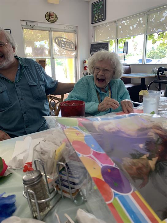 Two friends laugh together at a cafe table, enjoying each other's company and the warm atmosphere.