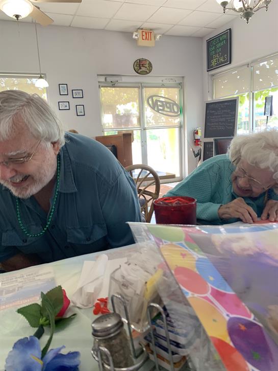 Elderly individuals and companions share engaging moments in a sunny arts workshop.