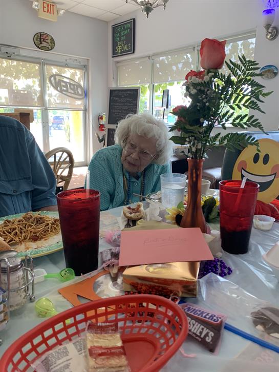 Seniors share a meal together, enjoying pasta and each other's company in a lively atmosphere.