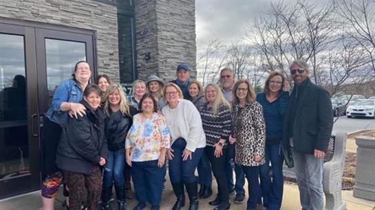 A diverse group of friends gathers outdoors, smiling and chatting together on a cloudy day.