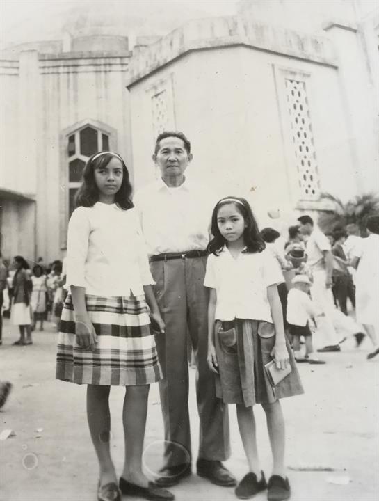 Two girls and a man stand together in front of a historic building during a cultural celebration.