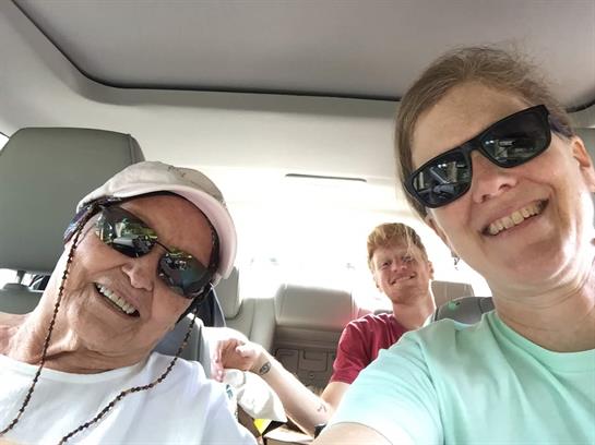 Three friends are smiling together inside a car, enjoying their time on a sunny day.