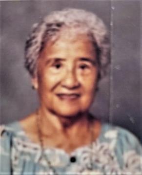 A smiling elderly woman in a blue floral dress exudes friendliness.