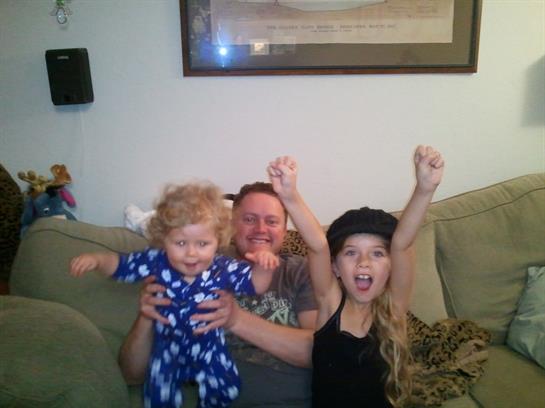 Two children celebrate happily while a parent holds a toddler on a comfortable sofa.