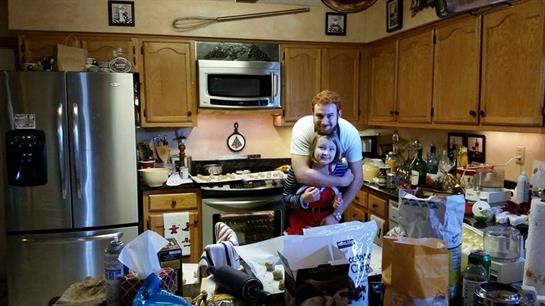 A father and daughter enjoy a joyful moment cooking in a festive, warm kitchen.