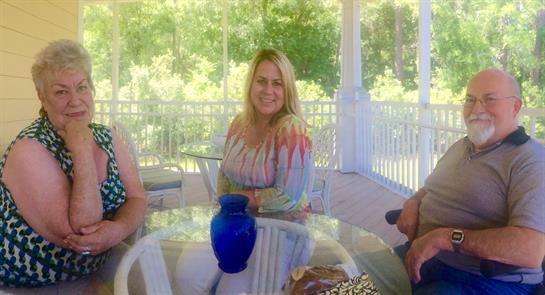 Three friends smile and relax on a sunny porch, enjoying drinks together.